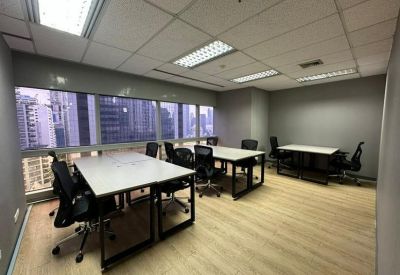 Bright open-plan office with three desks and city skyline views through large windows.