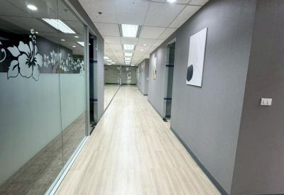 Long office corridor with grey walls, glass partitions, and recessed lighting.
