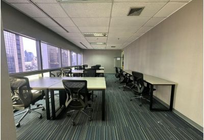 Shared office space with rows of desks and natural light from large perimeter windows.