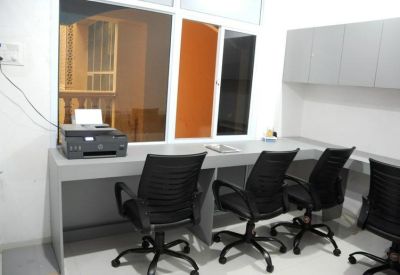 Shared office room with a long workstation, four black ergonomic chairs, and a desktop printer.