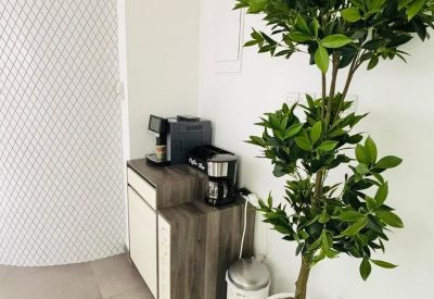 Communal coffee station with a sleek wooden cabinet and a large potted indoor tree.