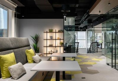 Modern breakout area with grey seating, yellow cushions, and a stylish backlit bookshelf.