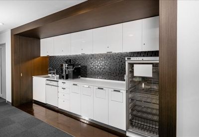 Modern office kitchen with white cabinetry, dark backsplash, and a wine fridge.