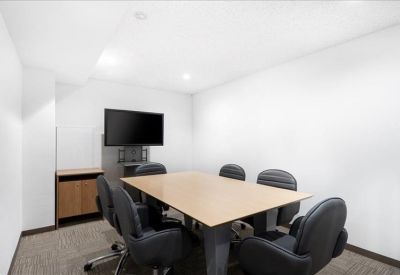 Private meeting room featuring a wooden table, wall-mounted screen, and black leather chairs.