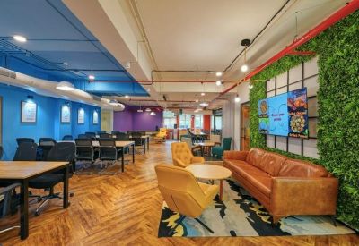 Vibrant breakout area with a tan leather sofa, plant wall, and colorful abstract rug.