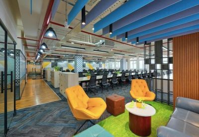 Lounge area featuring yellow tufted armchairs and a green turf rug near a long coworking desk.