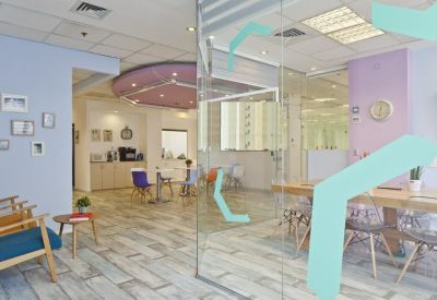 Breakout space with blue armchairs, small coffee tables, and a view into a private office area.