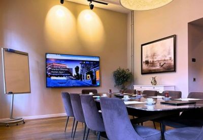 Spacious meeting room with a large screen, long table, and plush velvet chairs.