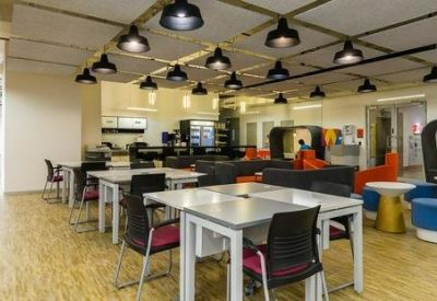 Bright coworking lounge with café-style seating, blue ottomans, and industrial pendant lighting.