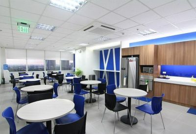 Bright office breakroom with white tables, blue chairs, and a small kitchenette.
