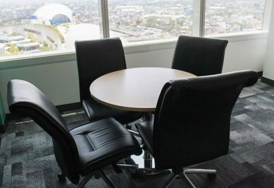 Small meeting area with a round table and four black leather chairs by a window.