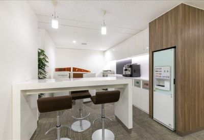 Communal kitchen and breakout area with high stools, a white counter, and a coffee machine.