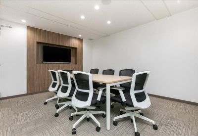 Bright meeting room with a wooden table, ergonomic chairs, and a wall-mounted television.
