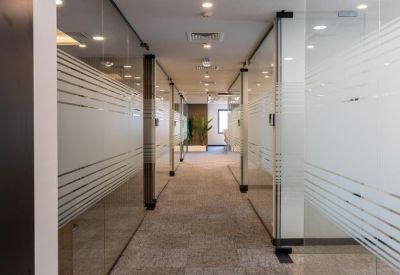 Long office corridor featuring frosted glass partitions and warm recessed lighting.