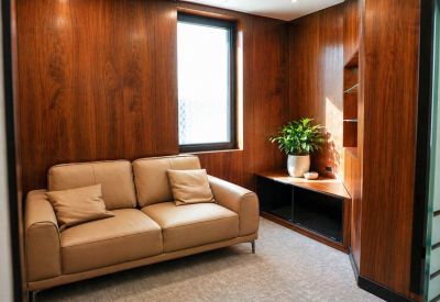 Cozy break area with a tan leather sofa, wooden walls, and a small potted plant near a window.