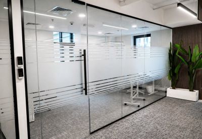 Modern glass-partitioned private office with frosted privacy strips and grey carpeting.