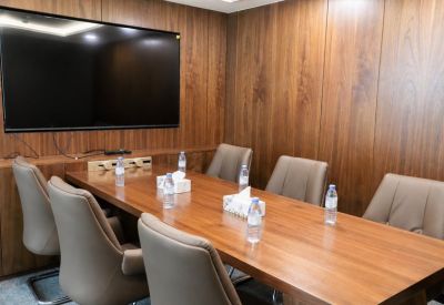Professional meeting room featuring a large wooden table, brown leather chairs, and a wall-mounted TV.