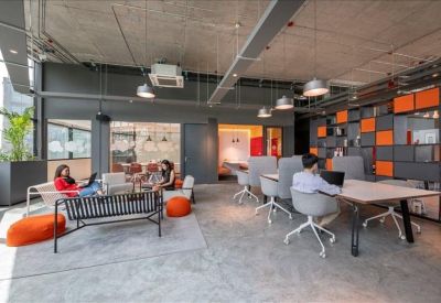 Open-plan coworking space with modern desks, ergonomic chairs, and vibrant orange accent stools.