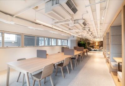 Long communal coworking table with wooden finishes and exposed ceiling pipes.