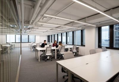Bright open-plan office space with long white desks and large windows.