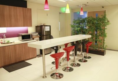 Communal break area with a long white breakfast bar, red stools, and lush indoor plants.