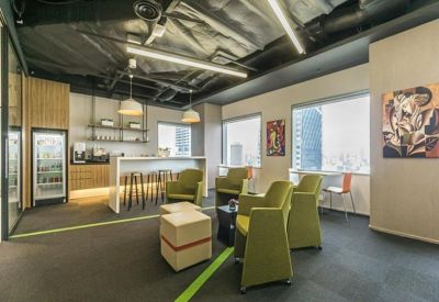 Spacious communal lounge with green armchairs and a breakout bar under an industrial ceiling.