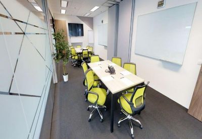 Meeting room with a central table, lime green chairs, and large whiteboards.
