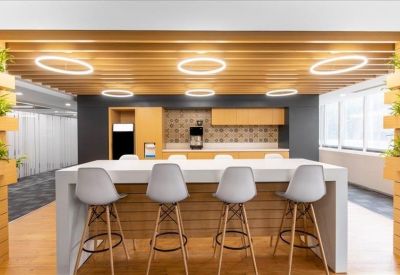 Communal break area with high-top seating, wooden ceiling baffles, and a modern kitchen unit.