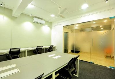Open-plan office with communal desks and a glass-enclosed meeting room.