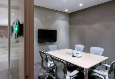 Modern meeting room with a wooden table, grey chairs, and a wall-mounted screen.