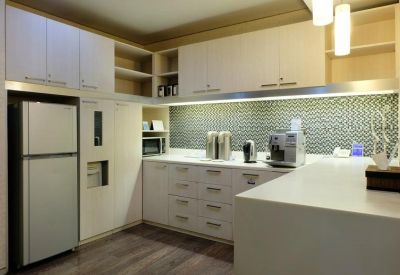 Modern communal kitchen area with sleek white cabinetry, a large fridge, and a breakfast bar.