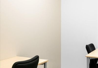 Compact two-person workspace with light wood desks and black ergonomic chairs.