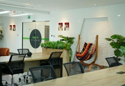 Casual meeting space with a striped hammock chair, wooden desks, and green plants.