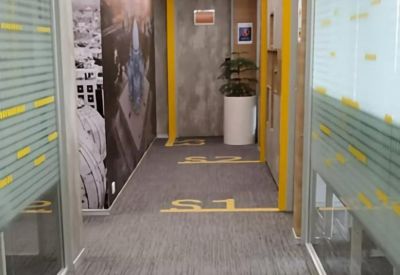 Modern office corridor with grey carpeting, wood slat ceilings, and glass-walled suites.