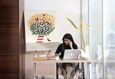 A professional sitting at a wooden desk with a large tree-themed painting on the wall.