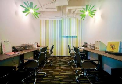 Coworking office area with multiple desks, ergonomic mesh chairs, and starburst-style ceiling lights.