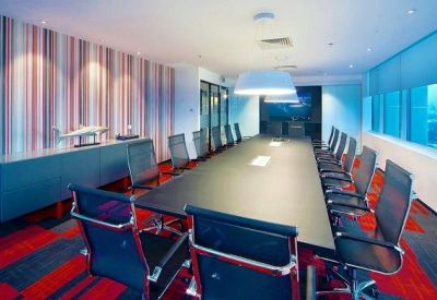 Long boardroom table in a meeting room with striped wallpaper and red patterned carpet.