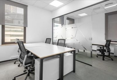 Bright glass-walled office with white desks and black ergonomic chairs.