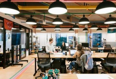 Open-plan workspace with long wooden desks under industrial black pendant lights.