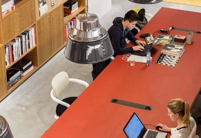 Coworking space with people working at a long red table under industrial pendant lights.