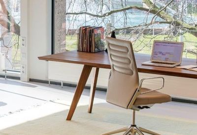 A wooden desk by a window with a leather office chair and tree views.