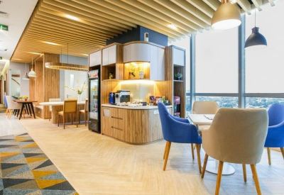 Bright communal kitchen and dining area with wooden slat ceiling and blue armchairs.