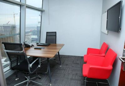 Private office with wooden desk, mesh chairs, and red guest seating overlooking the city.
