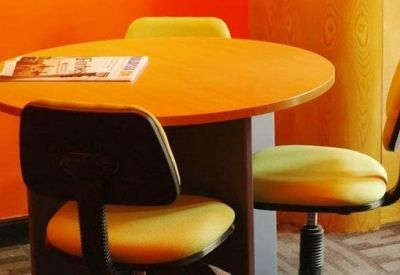 Small breakout area featuring a round orange table and lime green chairs against a vibrant orange wall.