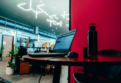 Desk setup with a laptop and water bottle against a bold red feature wall.