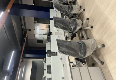 Modern open-plan workspace featuring rows of white desks and black ergonomic chairs in plastic wrap.