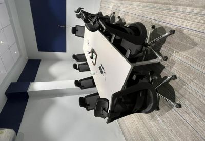 Conference room with a large white table, black mesh chairs, and striped carpet flooring.