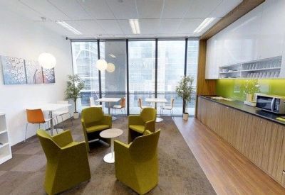 Communal breakroom with green lounge chairs, a kitchenette, and dining tables.