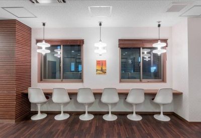 Long communal high-top desk with white swivel chairs and modern pendant lighting.