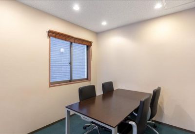 Professional four-person meeting room with a dark wood table and black leather chairs.
